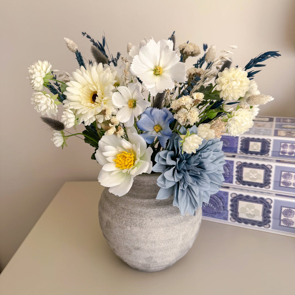 Bouquet of artificial flowers in a grey vase on a table with a patterned box in the background.