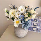 Bouquet of artificial flowers in a grey vase on a table with a patterned box in the background.