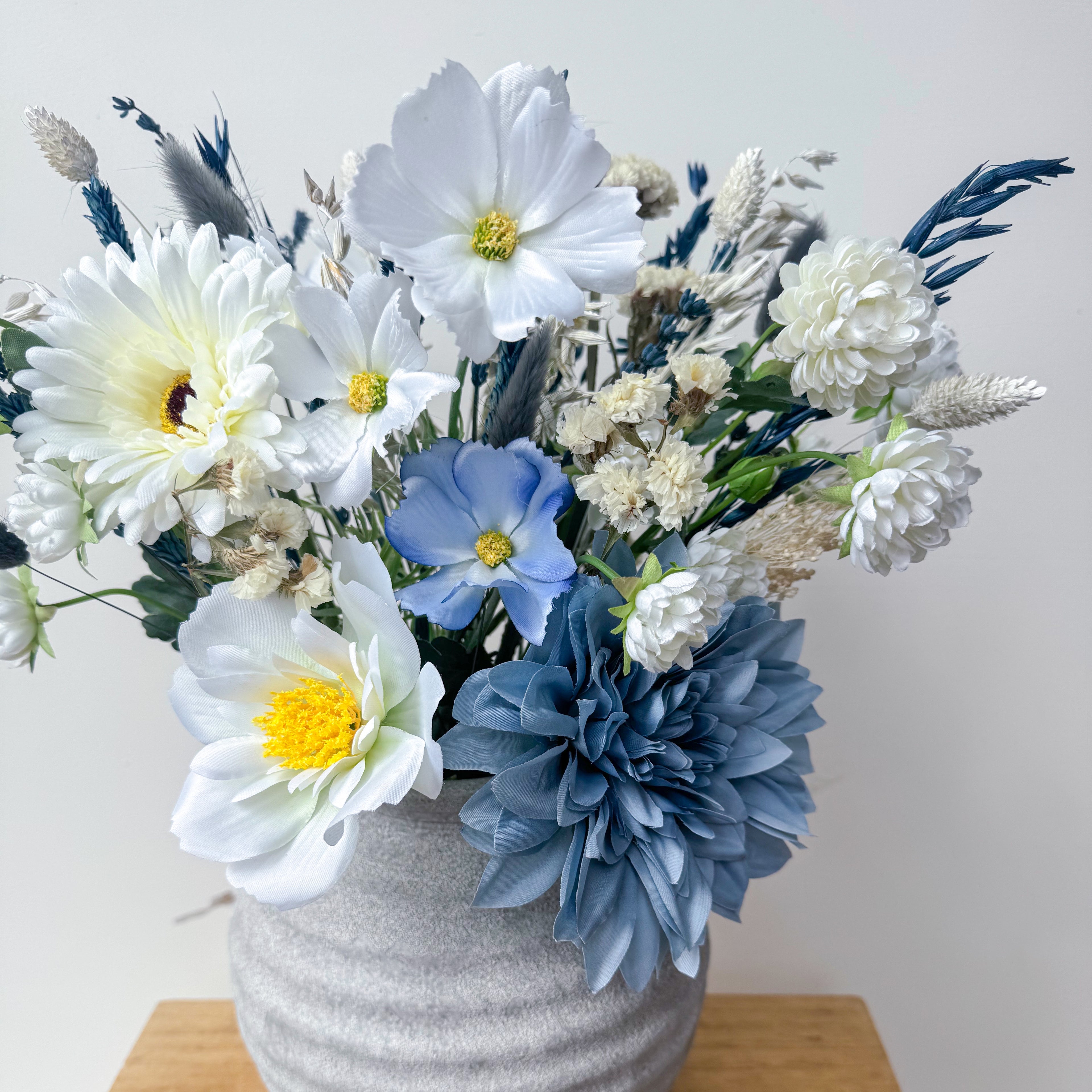 Bouquet of white and blue flowers in a textured vase on a light background