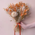 a peach coloured dried flower arrangement with gypsophila, wheat and oats against a plain background