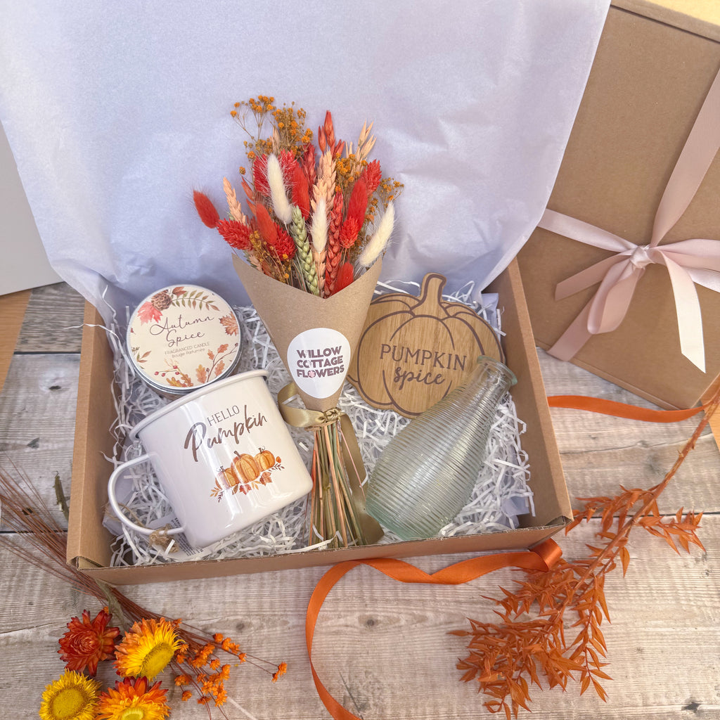 an autumn themed gift box with pumpkin mug, autumn spice candle, burnt orange flowers, wooden pumpkin shaped coaster and glass vase