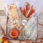 an autumn themed gift box with orange dried flowers, autumn spice scented tea lights, orange pumpkin candle holder and glass vase.