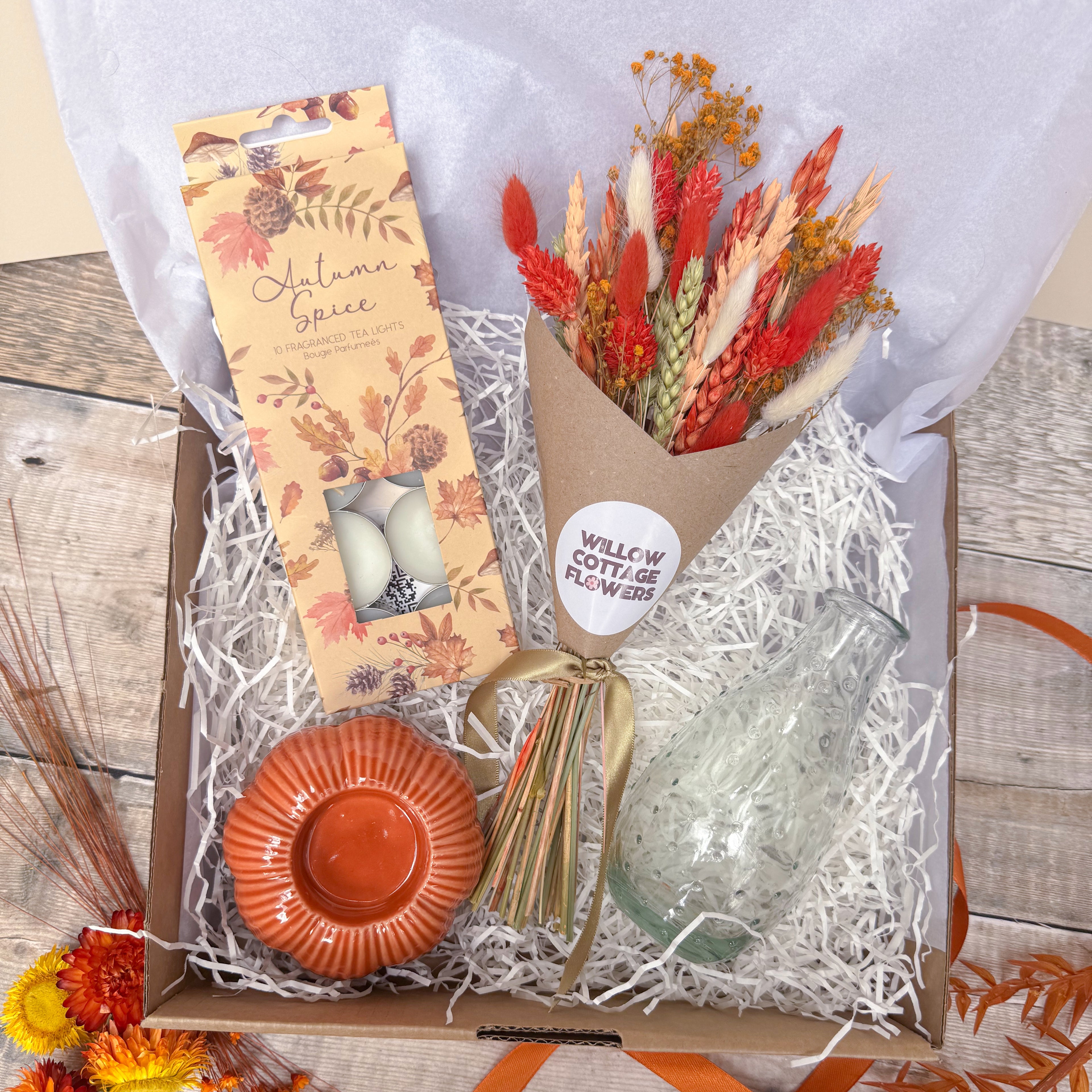 an autumn themed gift box with orange dried flowers, autumn spice scented tea lights, orange pumpkin candle holder and glass vase.