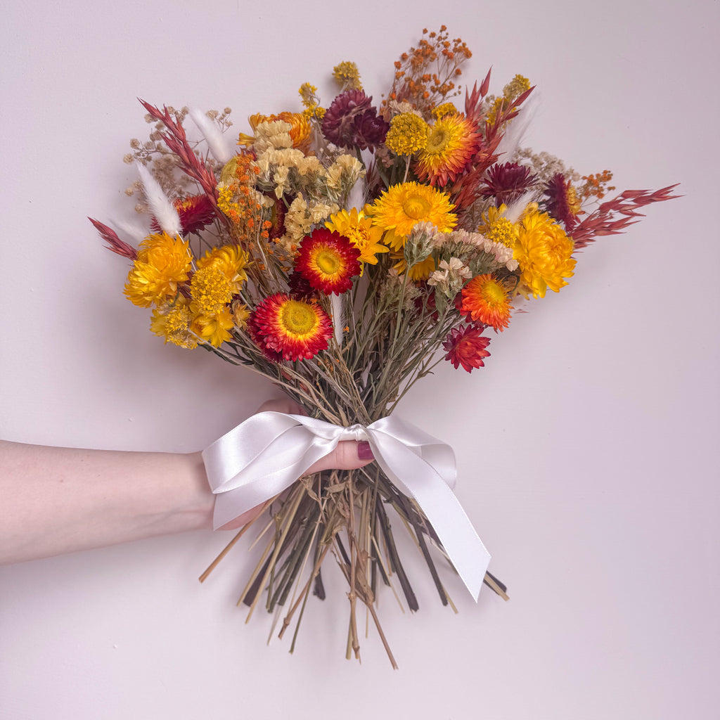 Bouquet of colorful flowers with a white ribbon held by a hand on a light background