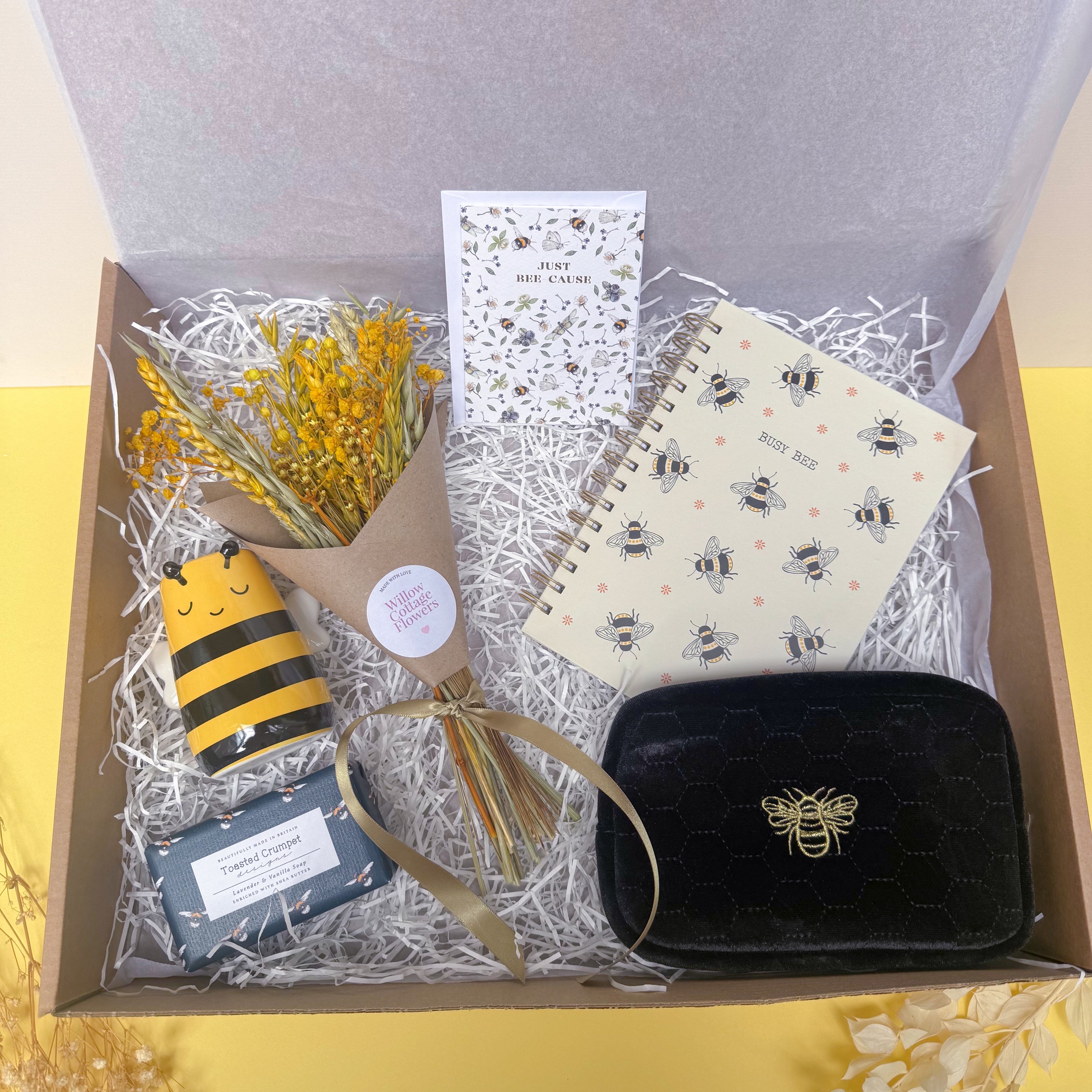 Gift set with bee-themed items including a notebook, cosmetics bag and card in a box.