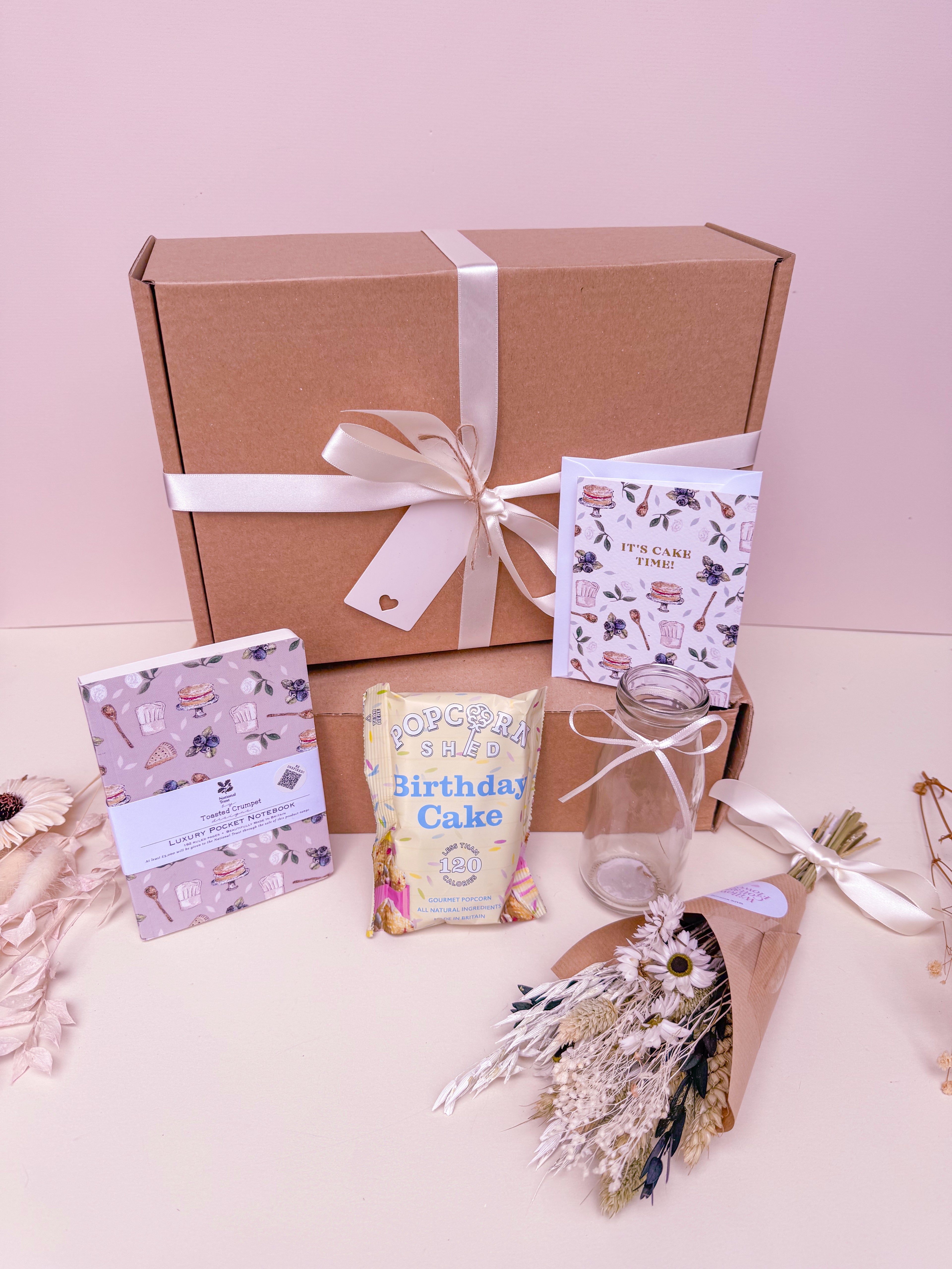 Gift box with a bow, birthday card, and birthday themed gifts on a light pink background