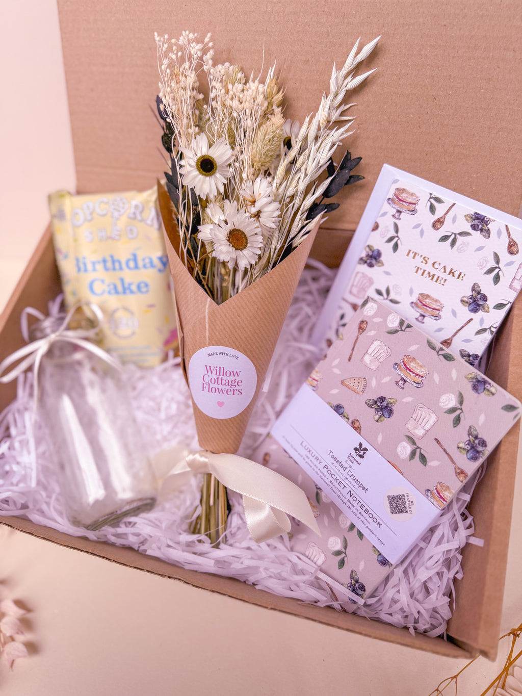 Gift box with a bouquet of flowers, a vase, and stationery items on a light pink background