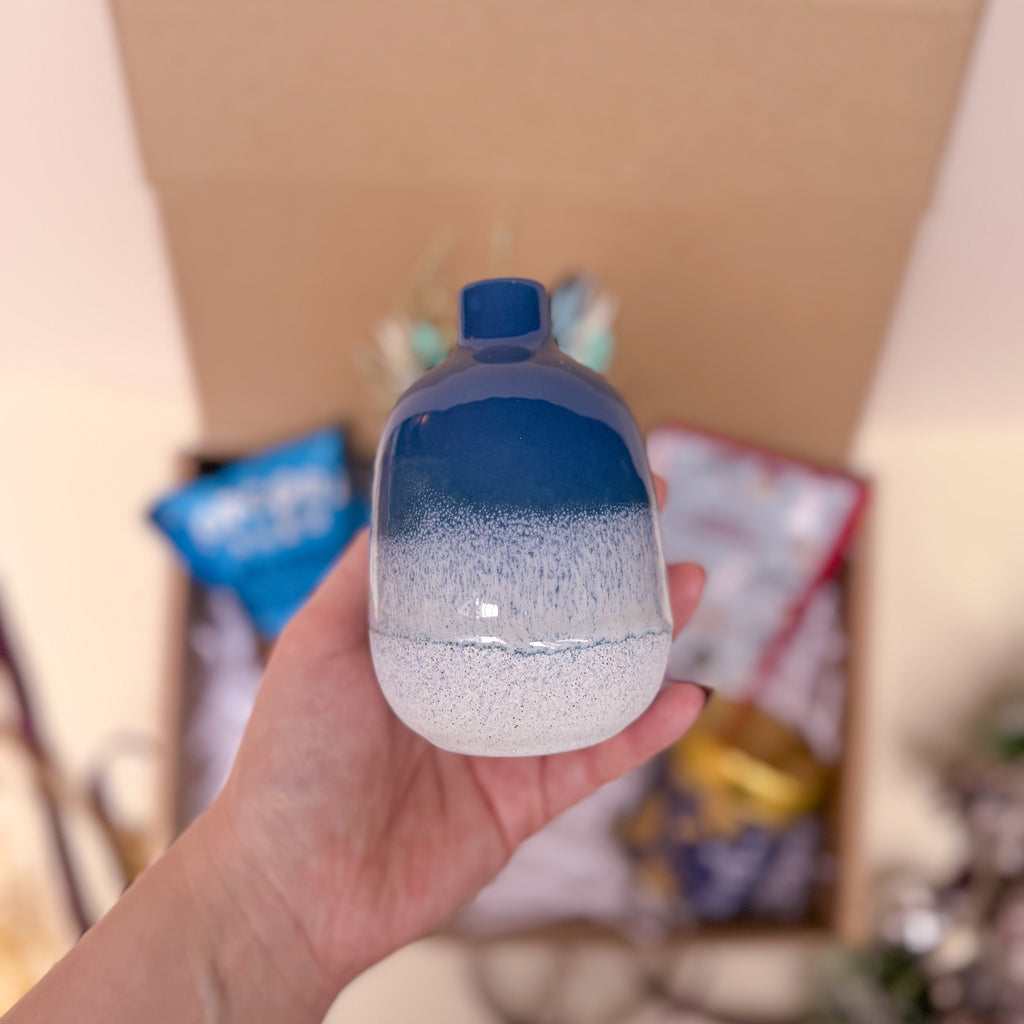 Hand holding a small gradient blue vase against a blurred background