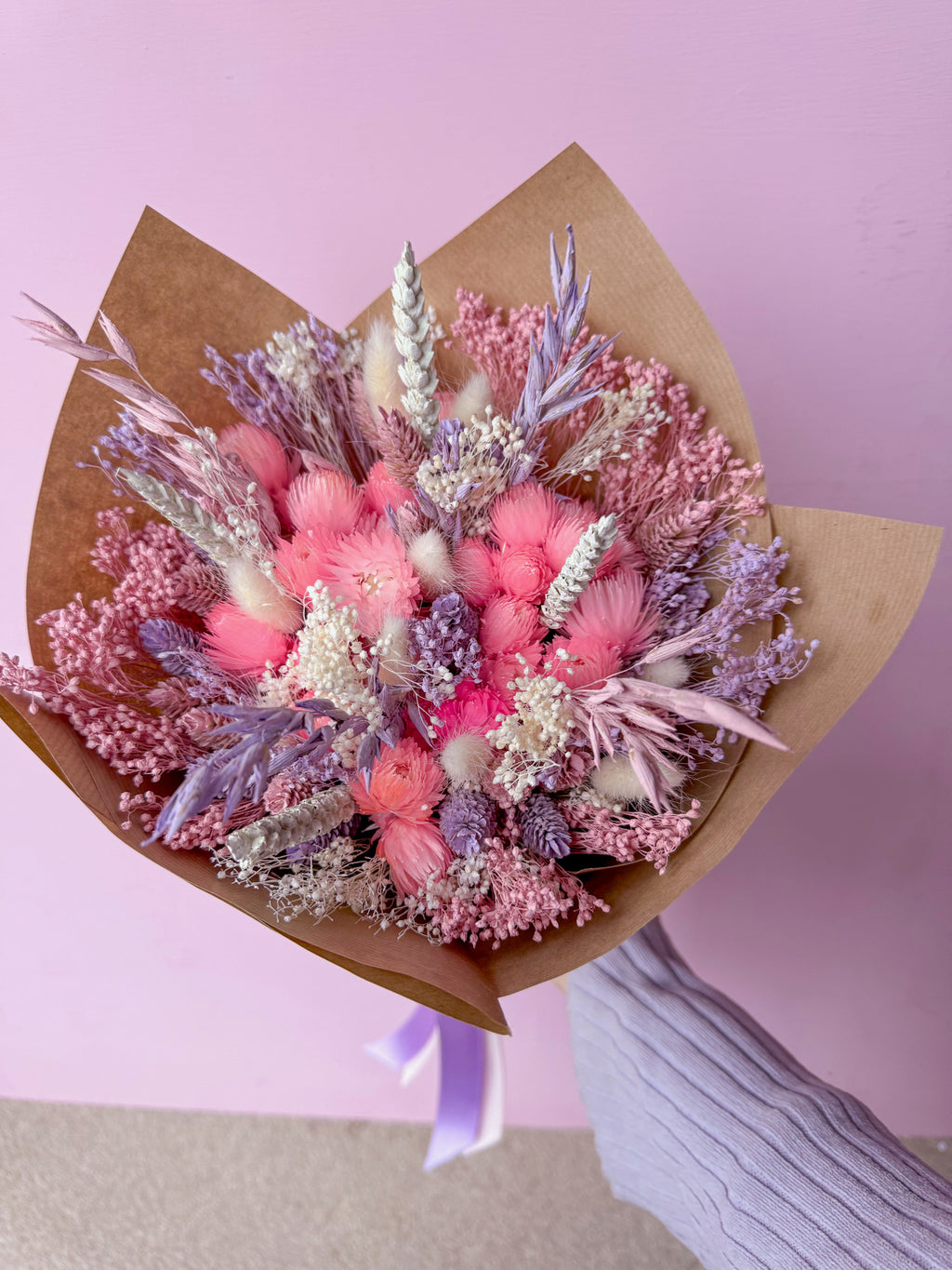 Bouquet of pink and purple flowers wrapped in brown paper against a pink background