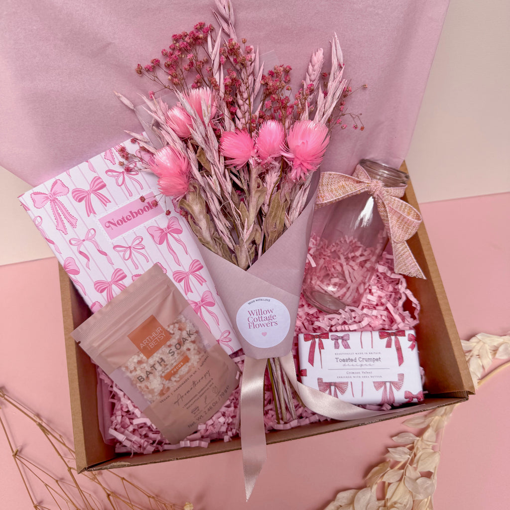 Gift box with pink flowers, a glass vase and a notebook on a pink background