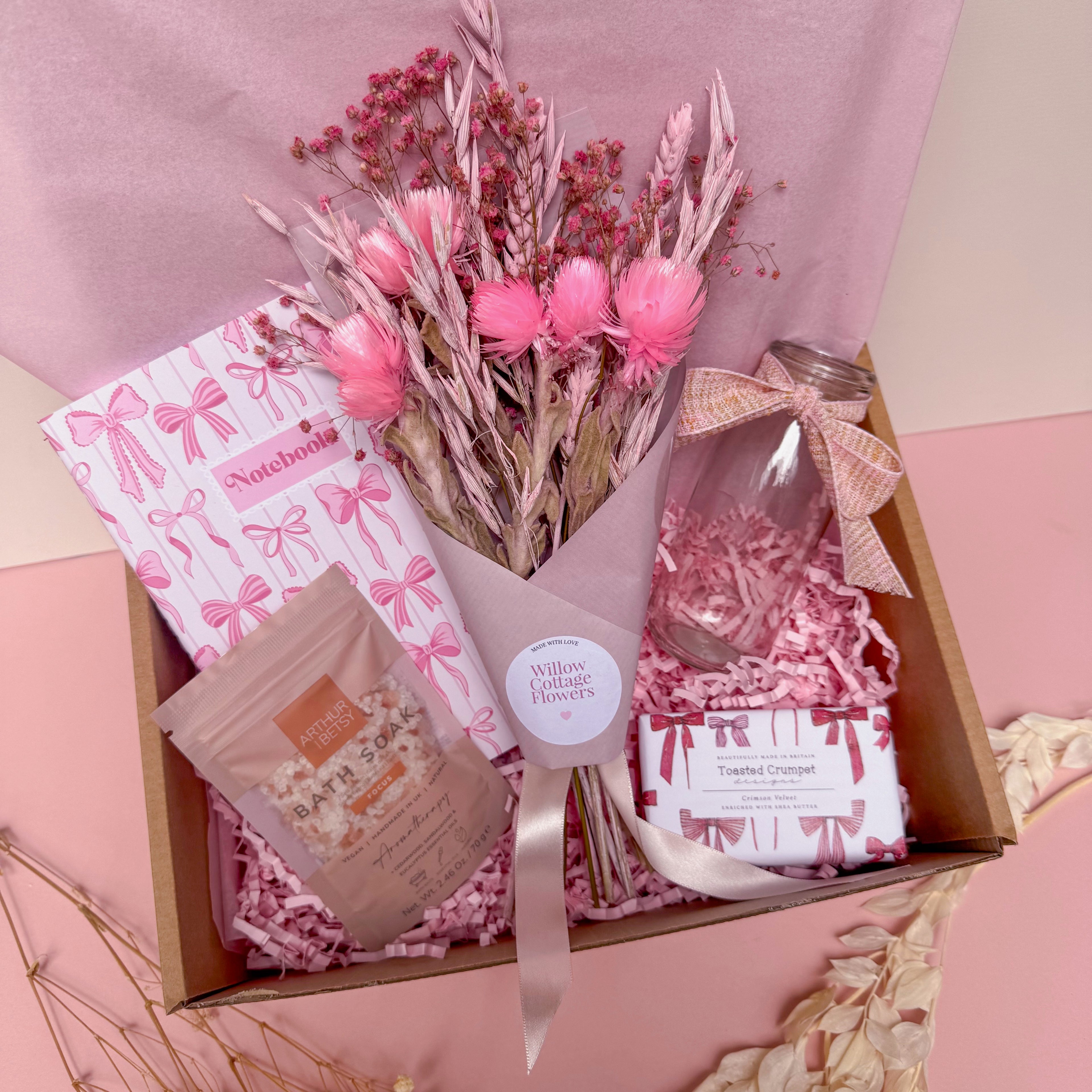 Gift box with pink flowers, a glass vase and a notebook on a pink background