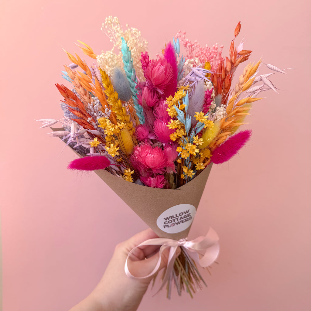 colourful rainbow dried flower bunch being held against a pink background