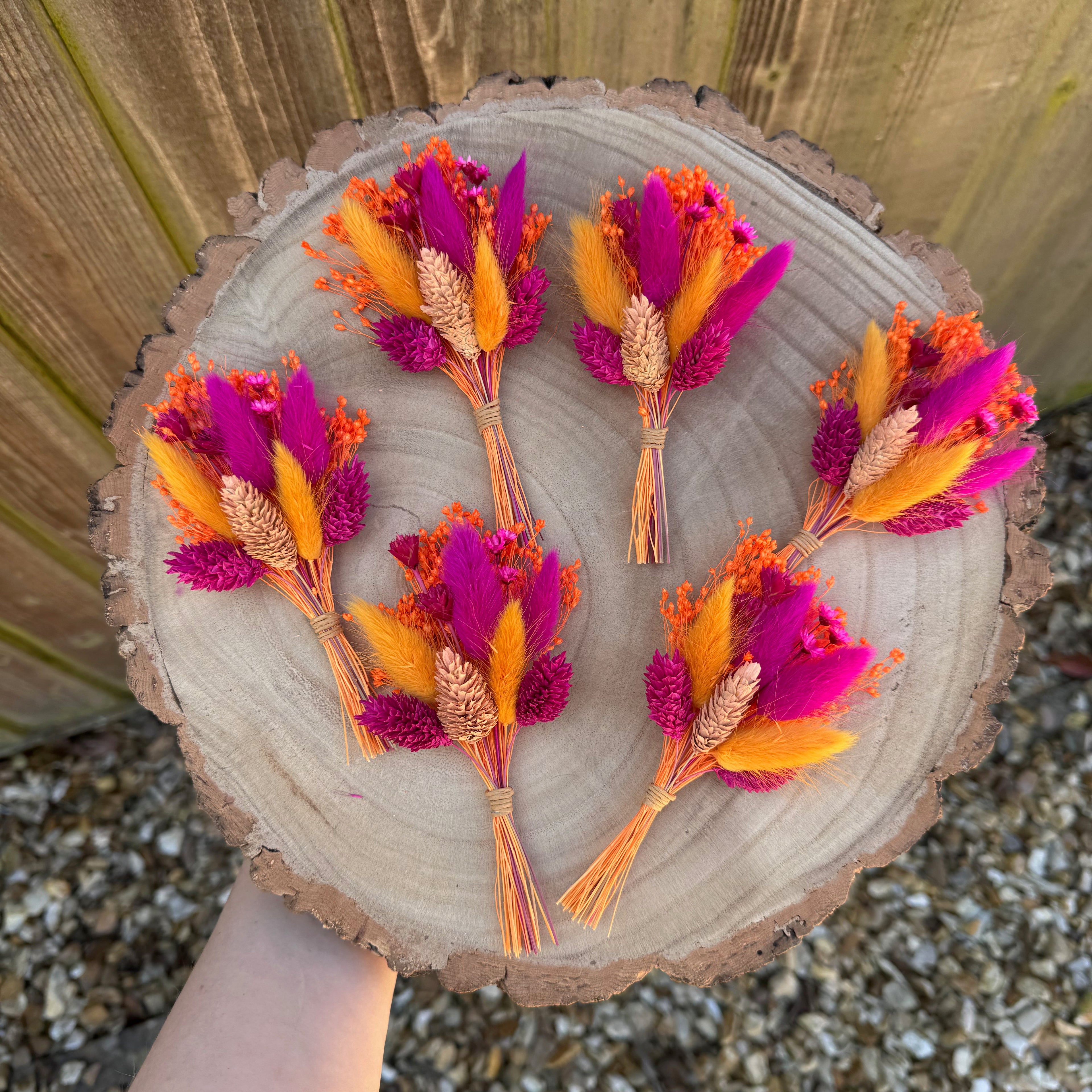 bright orange and hot pink dried flower buttonholes displayed on wood background