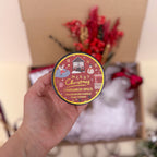 Hand holding a cinnamon spice candle with a festive design against a blurred background