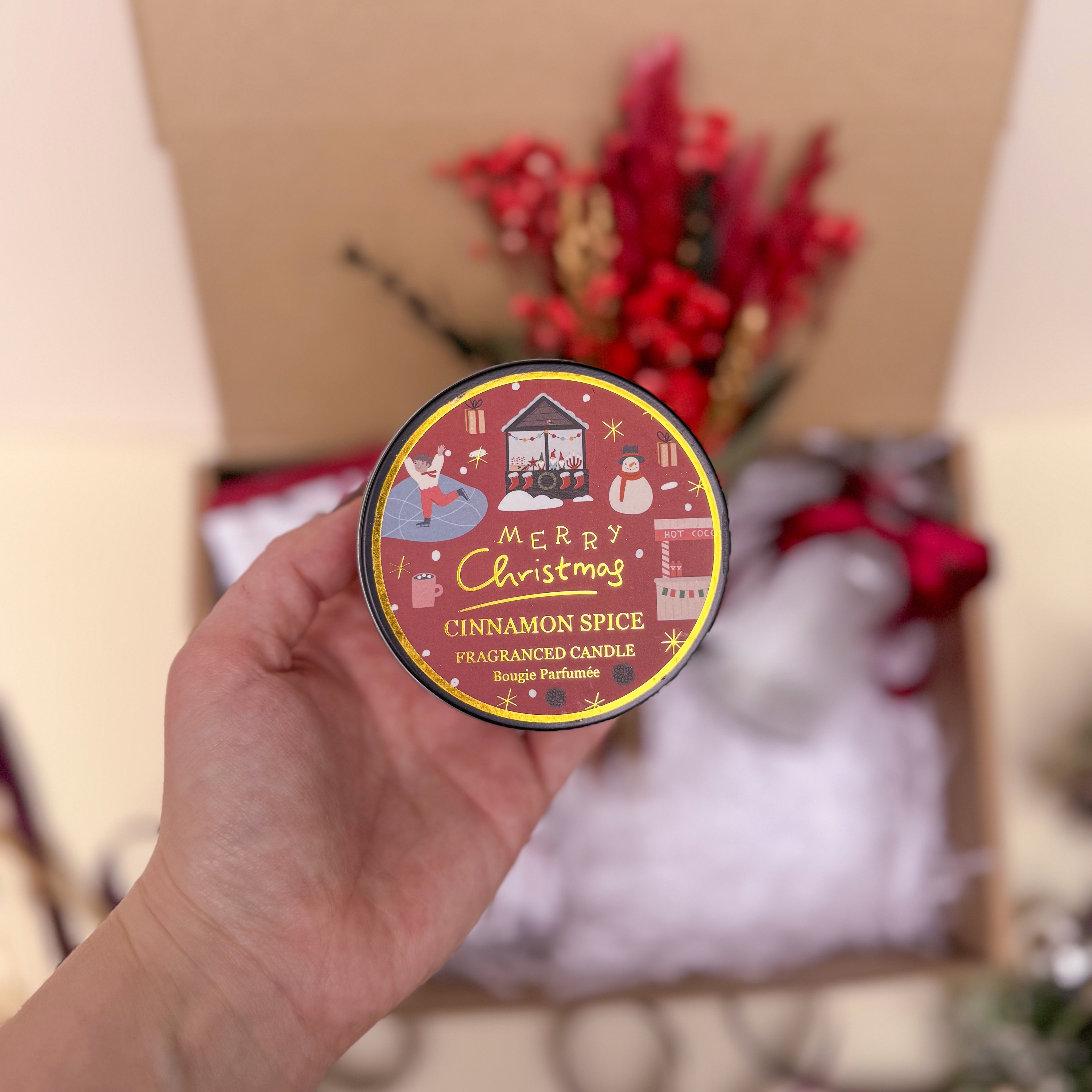 Hand holding a cinnamon spice candle with a festive design against a blurred background