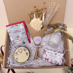 Gift box with flowers, candles, and other festive items on a light background