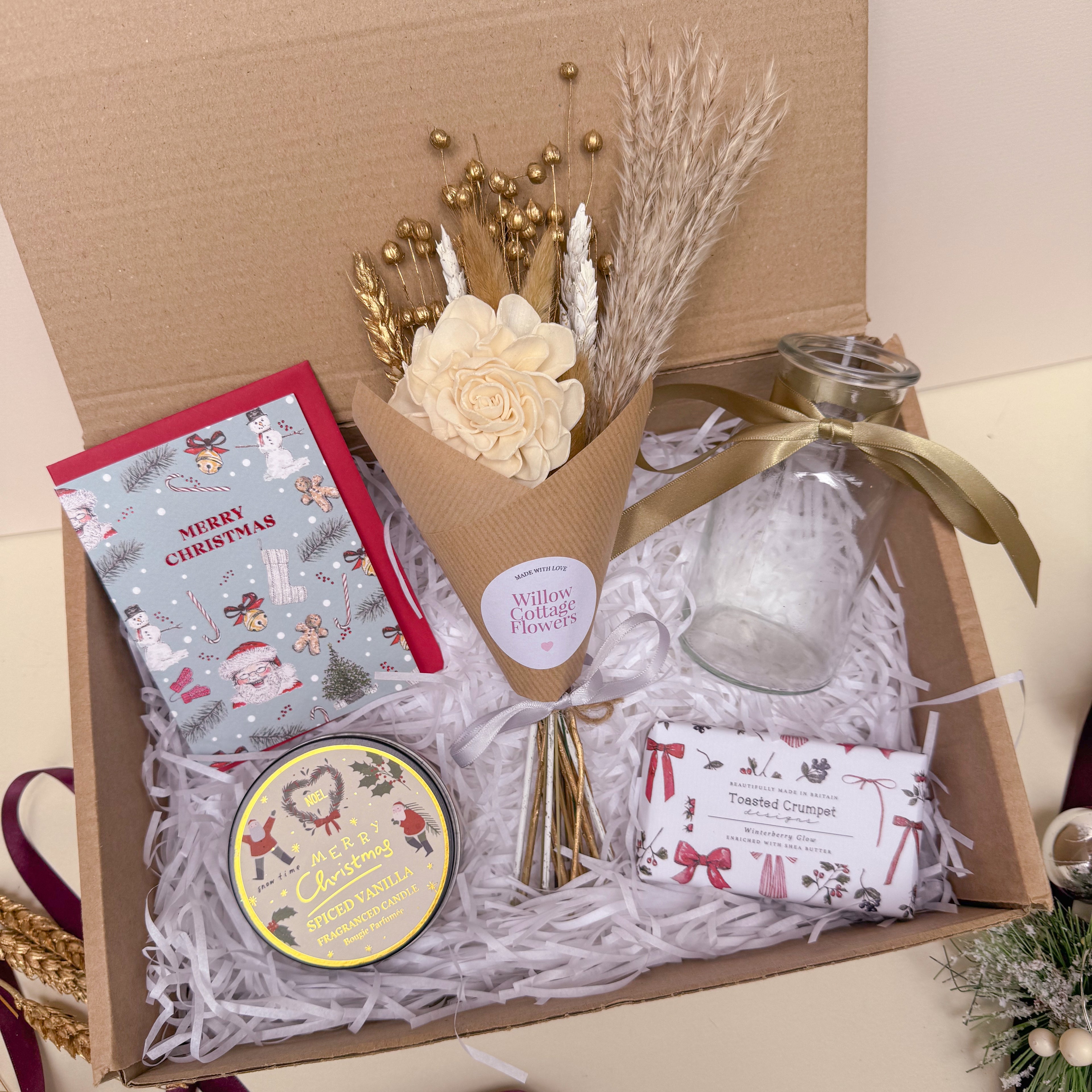 Gift box with Christmas-themed items including a bouquet, candle, and soap.