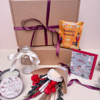 Gift box with festive items including a bouquet, candle, and card with a ribboned gift box