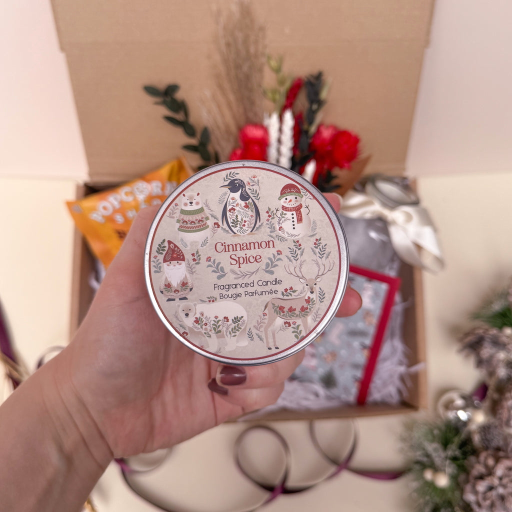 Hand holding a cinnamon spice candle with decorative label, Christmas-themed background