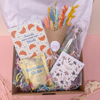 Gift box with stationery items, flowers, and a card on a pink background for birthday