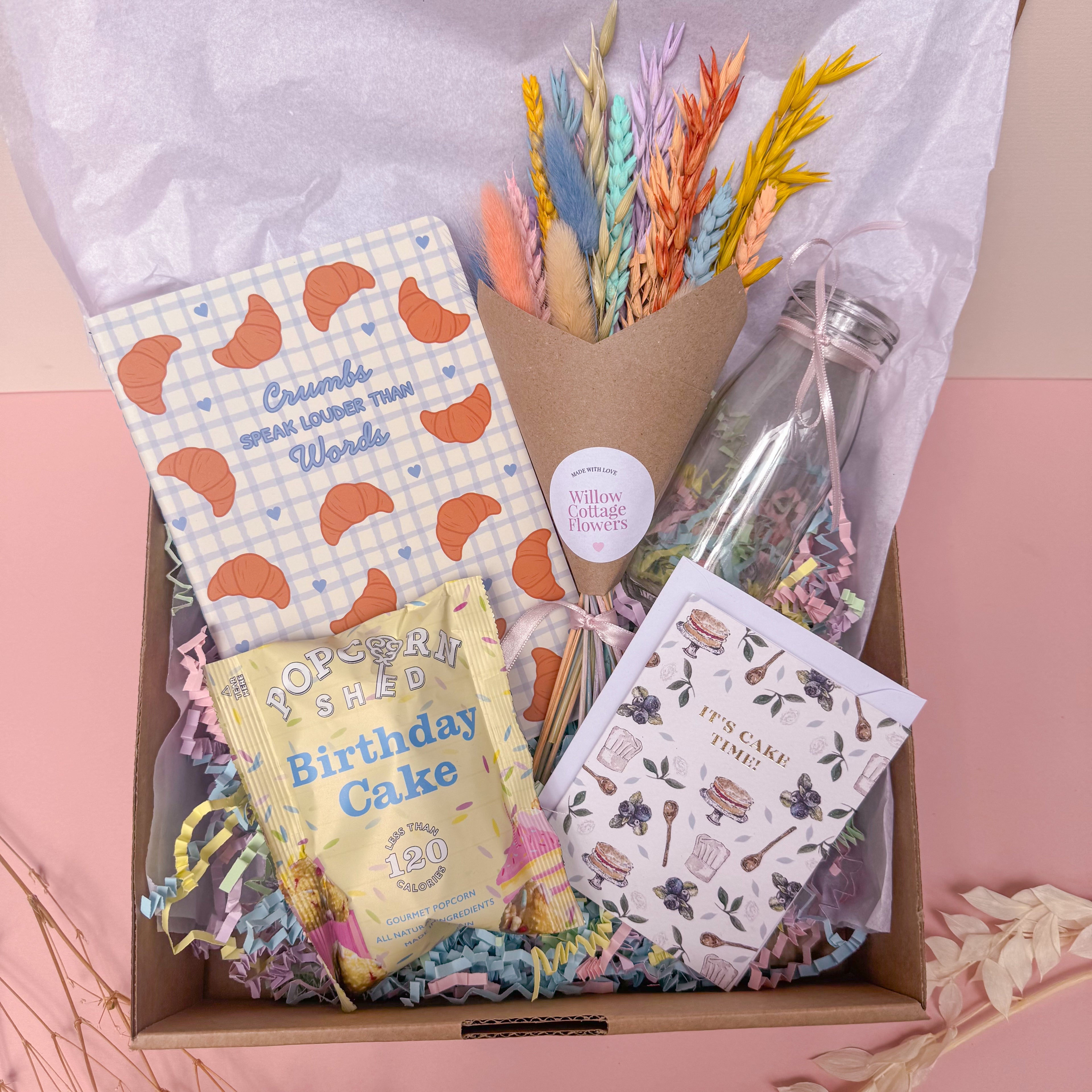 Gift box with stationery items, flowers, and a card on a pink background for birthday