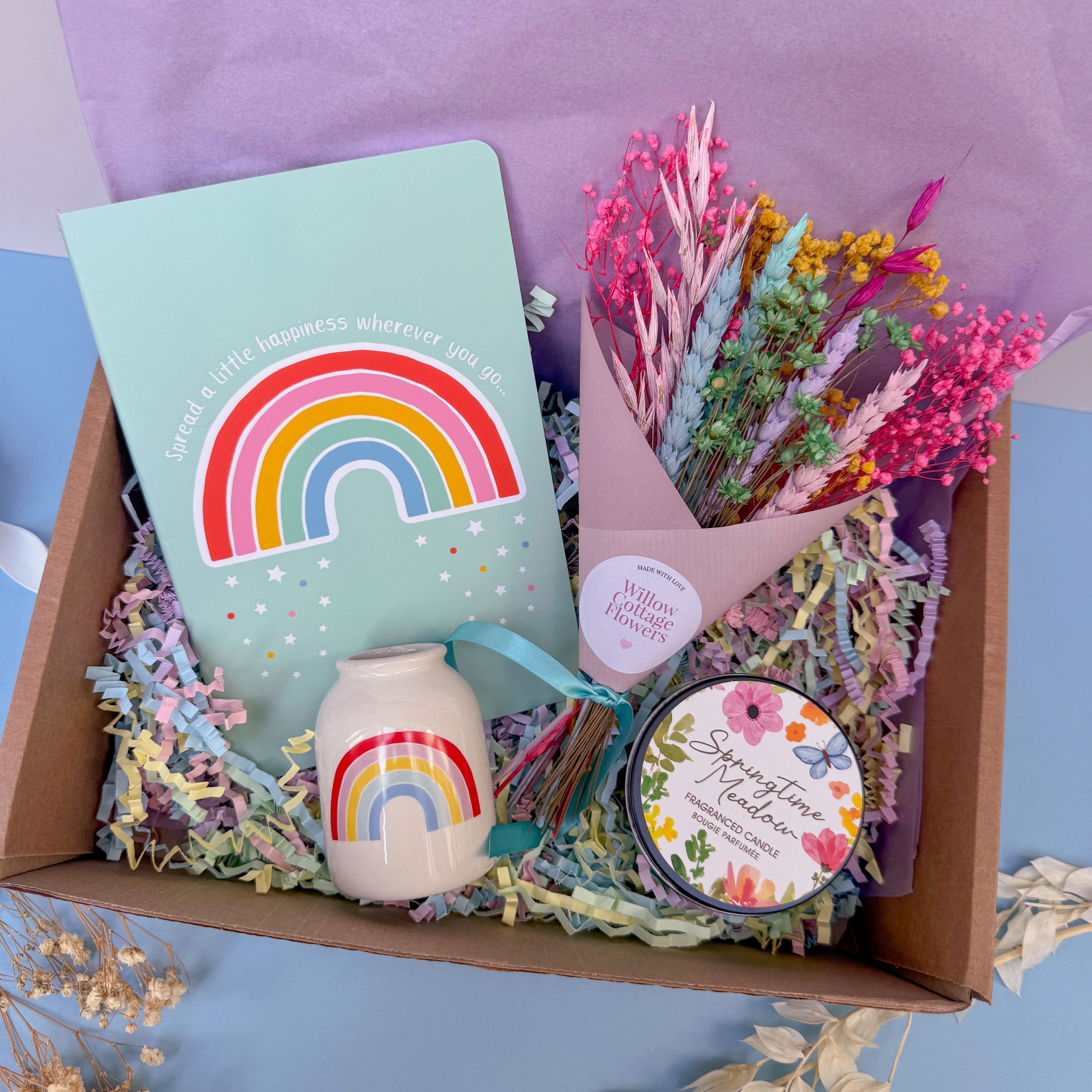 Gift set with rainbow-themed items including a vase, notebook, and flowers in a box.