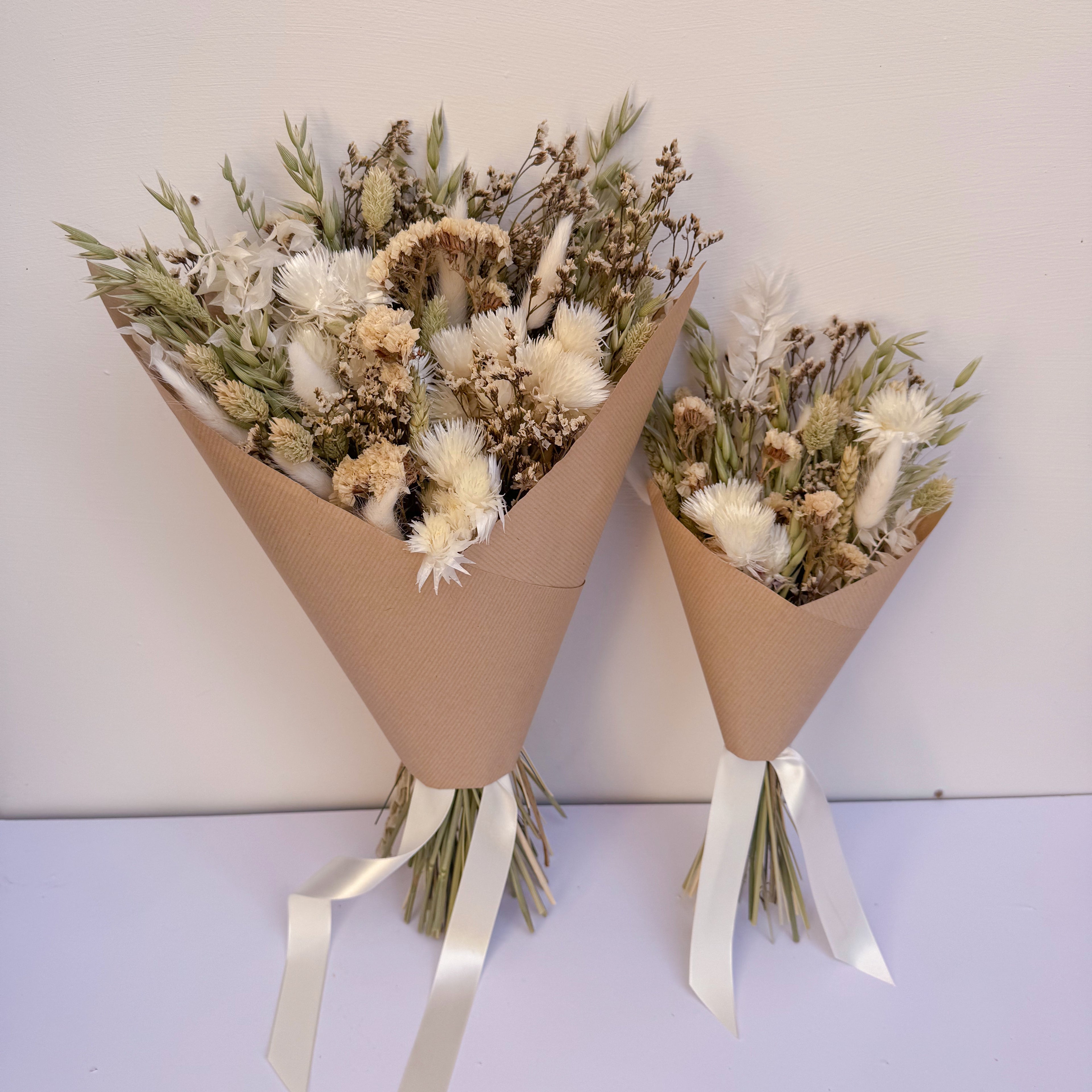 Two bouquets of green dried flowers wrapped in brown paper with white ribbons on a light background