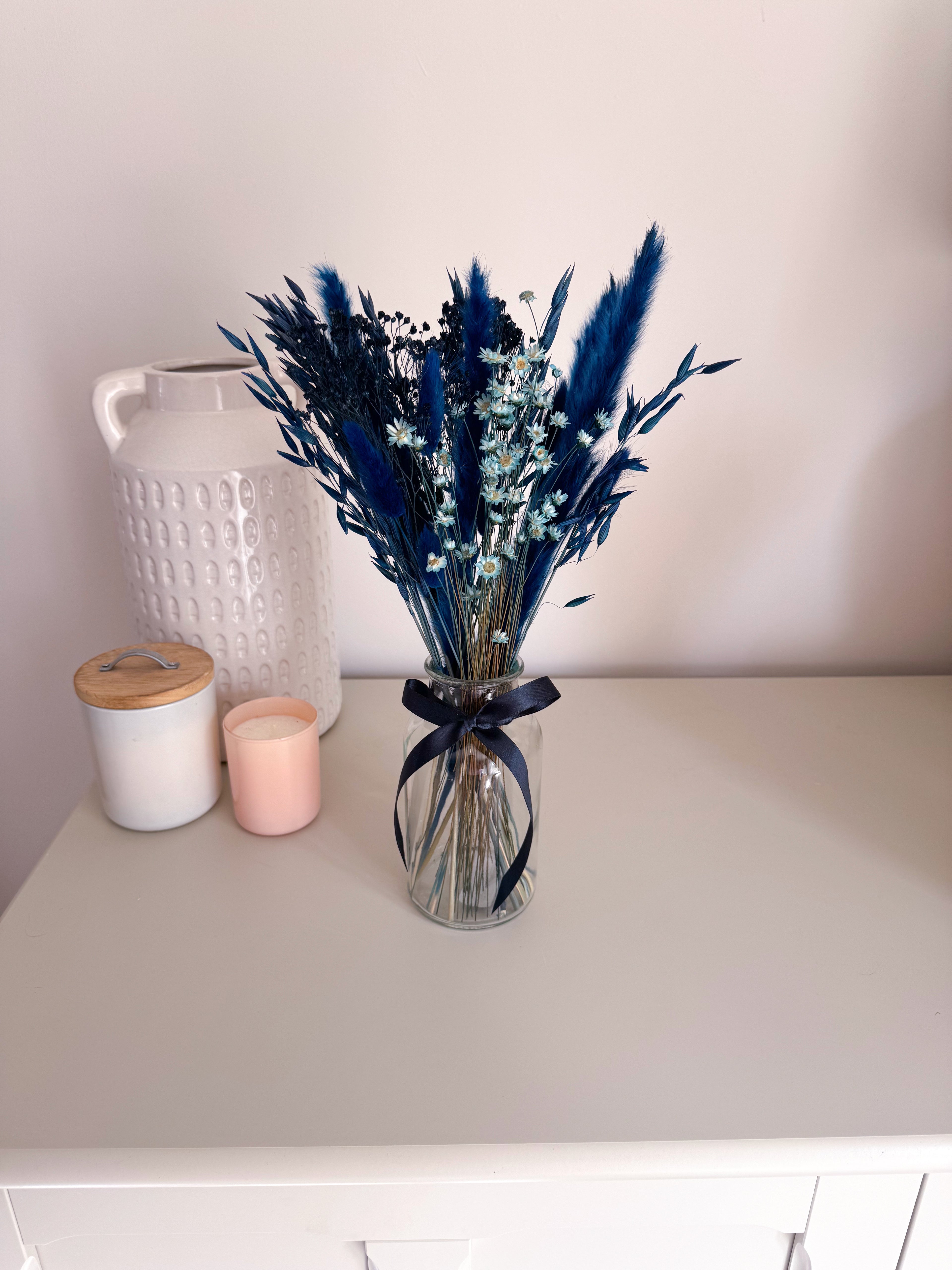 navy pampas grass bouquet in glass vase with navy ribbon displayed on a white table with other home decor items