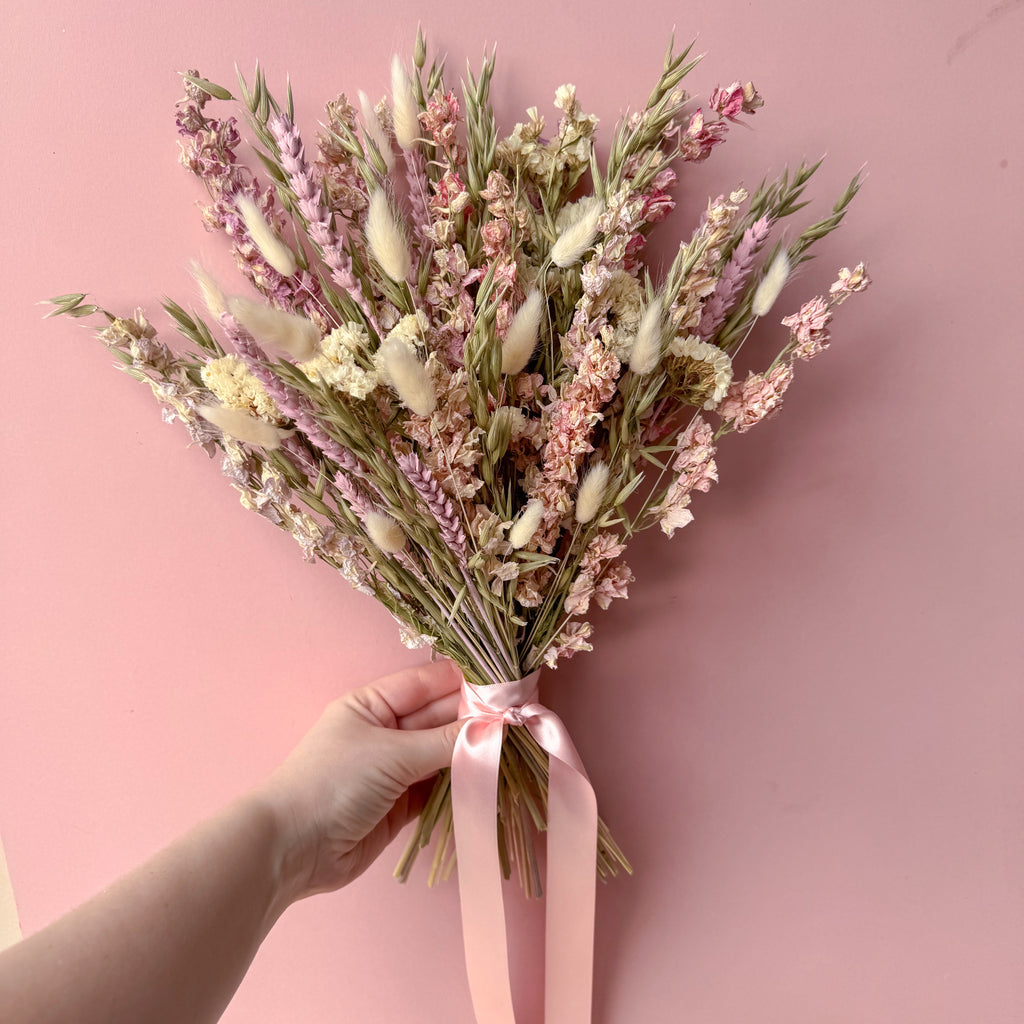 a pink delphinium arrangement being held against a pink background
