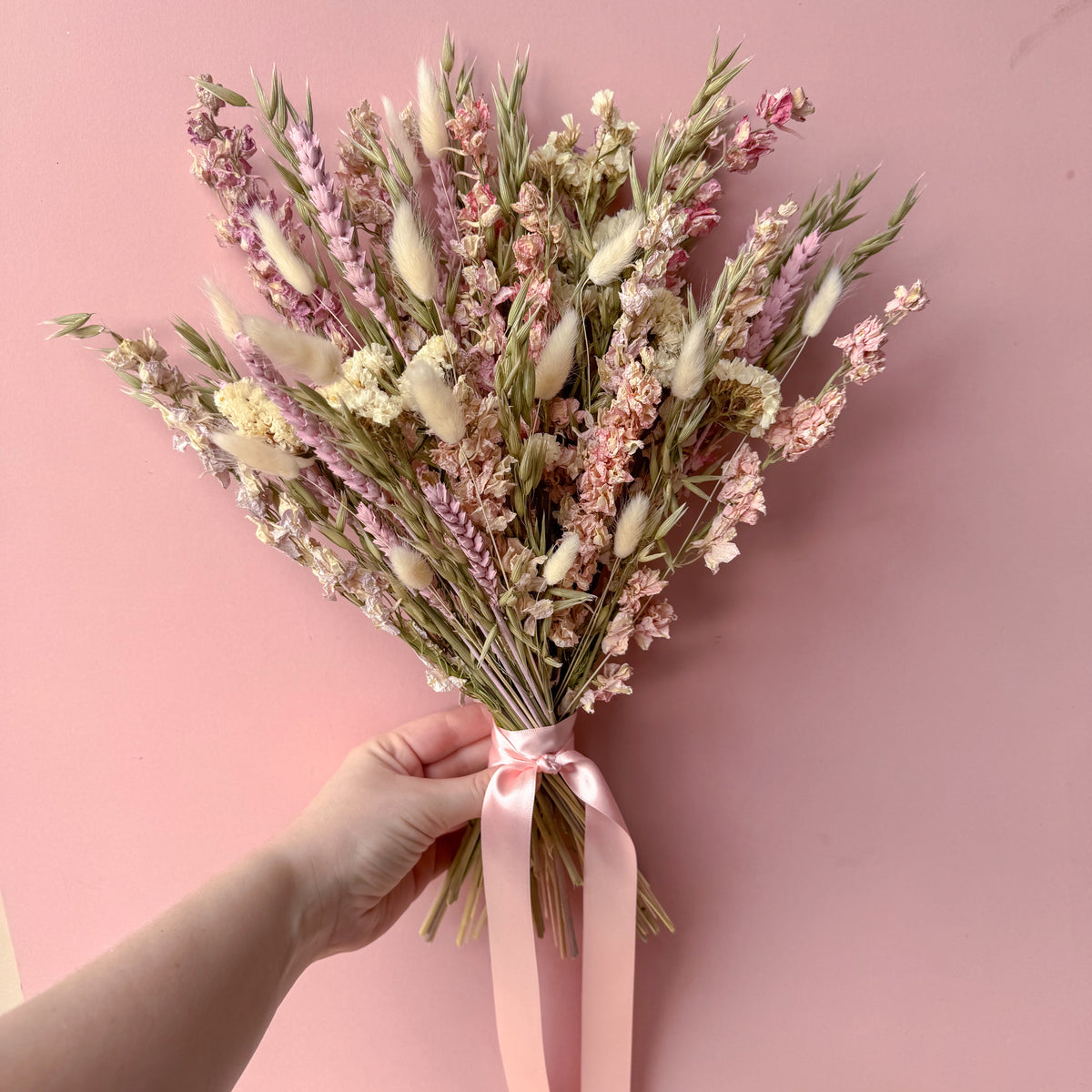 a pink delphinium arrangement being held against a pink background