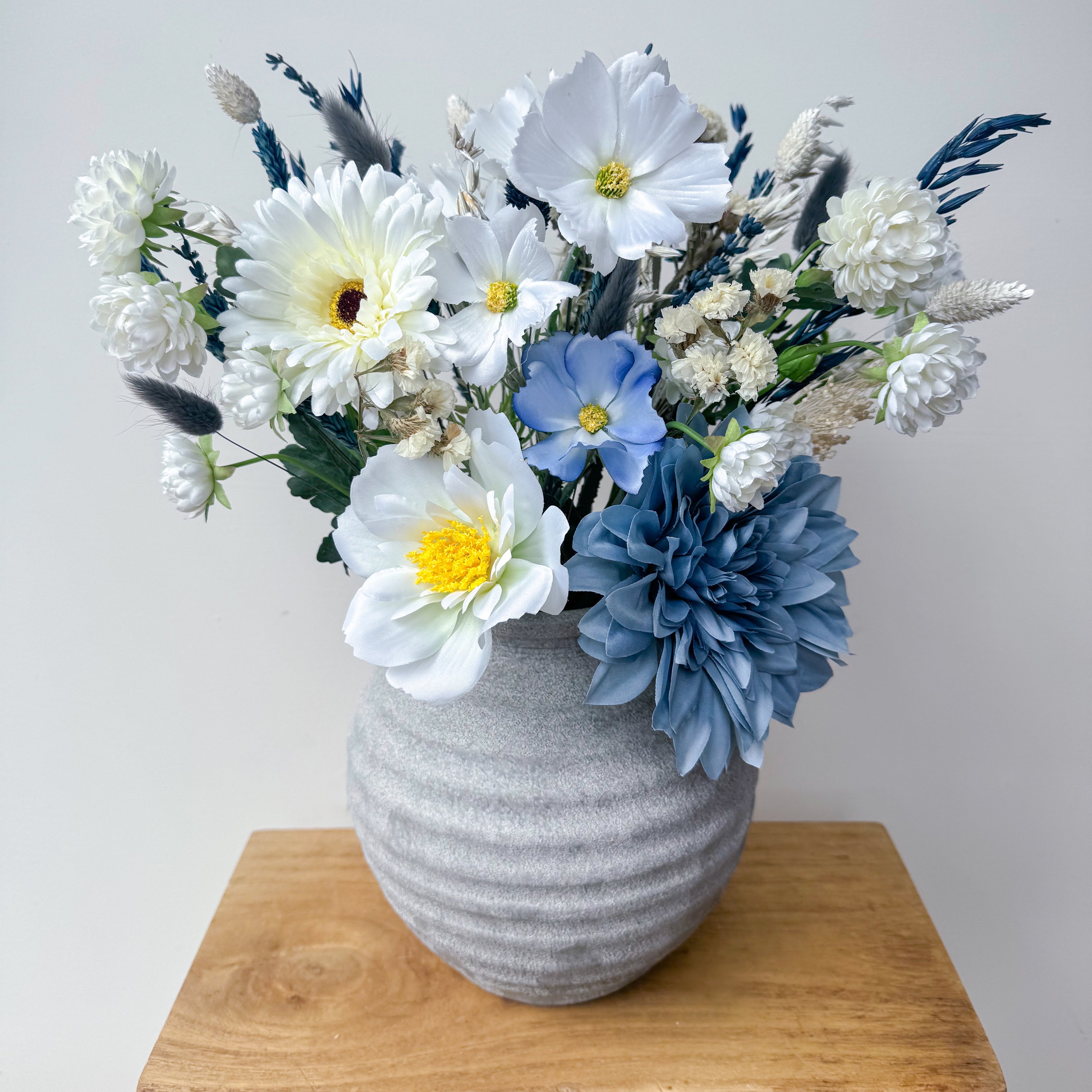 Gray textured vase with a bouquet of white, blue, and yellow artificial flowers on a wooden surface.