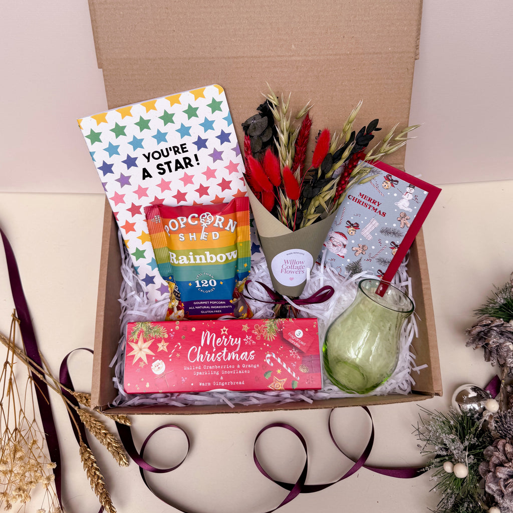 Gift box with festive items including a card, popcorn, and a candle on a white background.