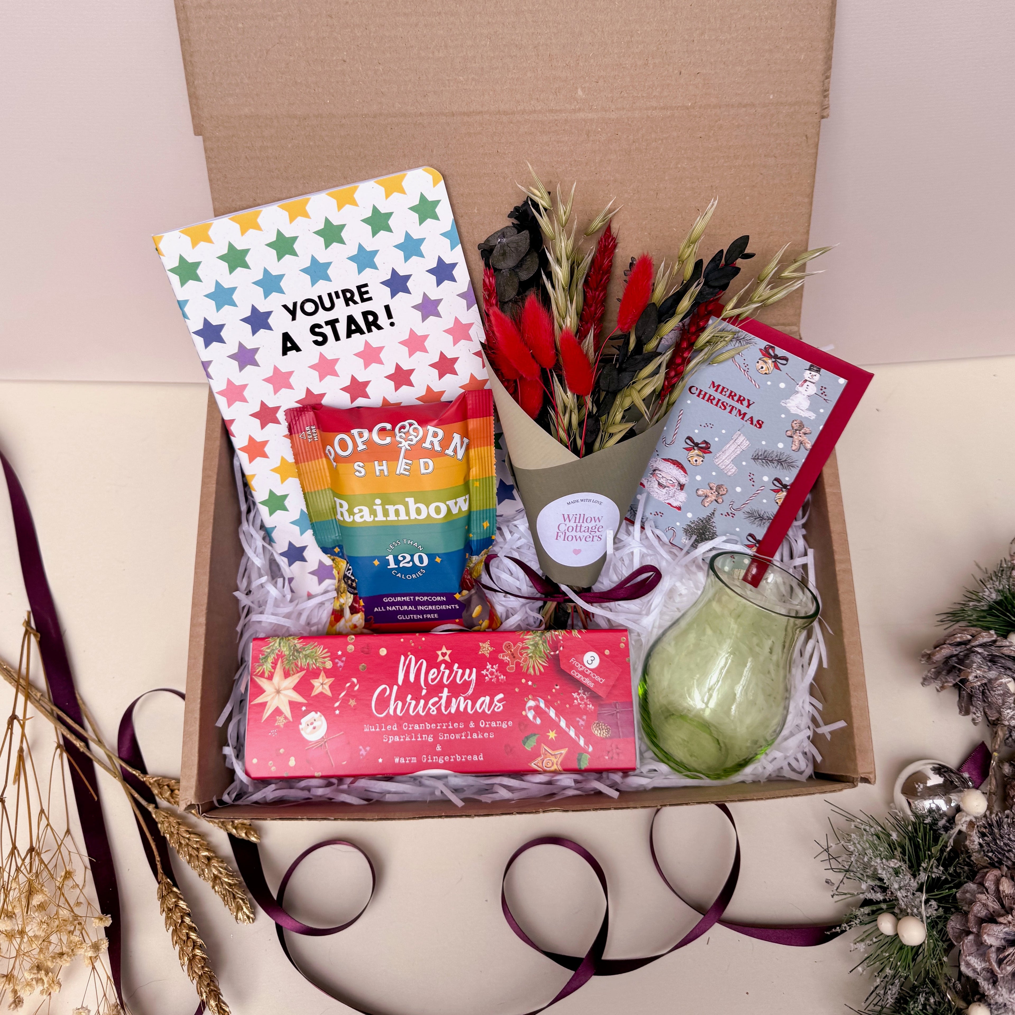 Gift box with festive items including a card, popcorn, and a candle on a white background.