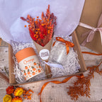 a curated gift box with an orange theme, containing orange scented candle, orange dried flowers and glass vase with orange ribbon