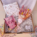 Gift box with dried flowers, strawberry scented candle, popcorn and a giraffe card on a light background