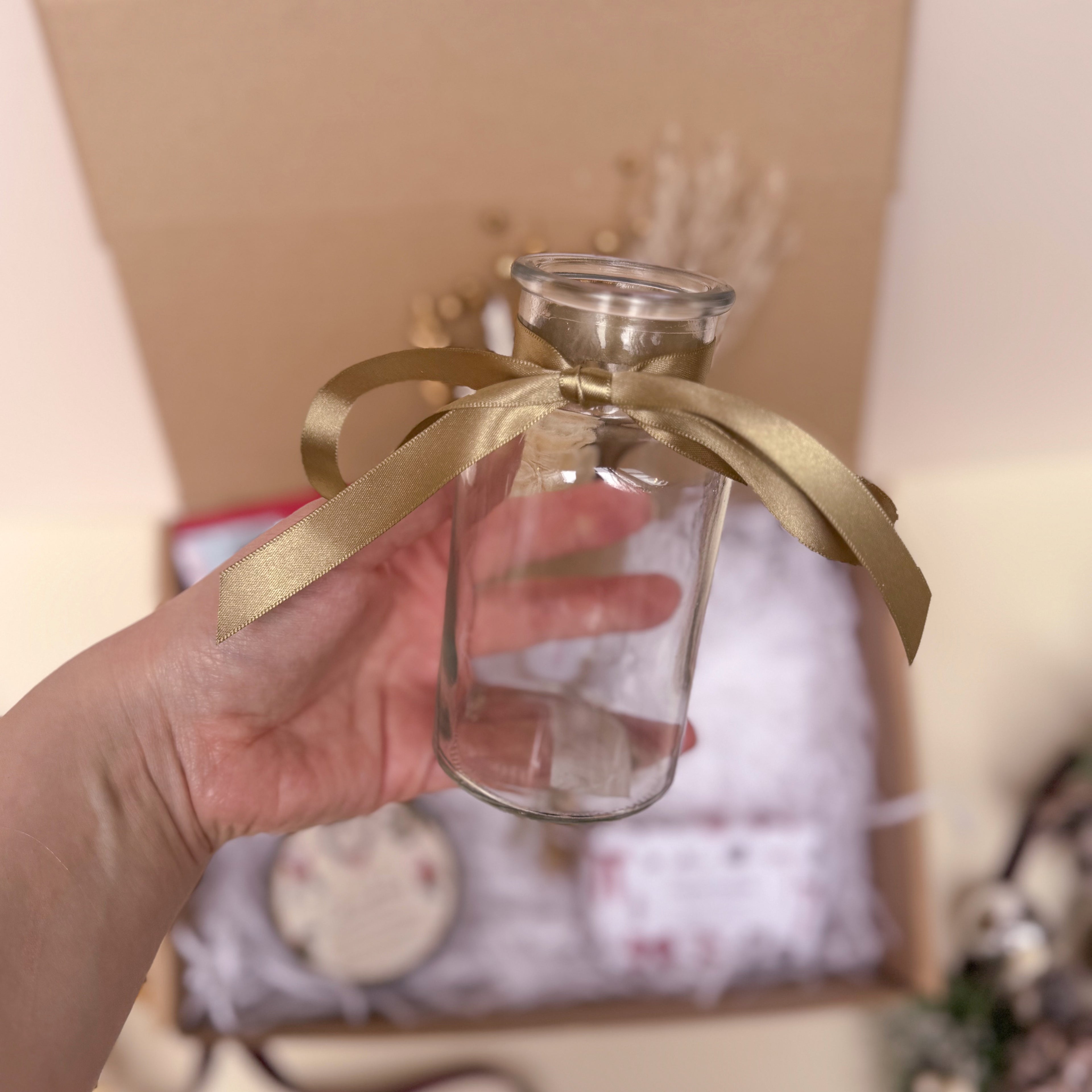 Clear glass vase with a gold ribbon held by a hand against a blurred indoor background
