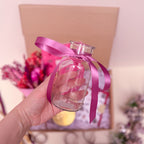 Clear glass bottle with a pink ribbon held by a hand against a blurred background