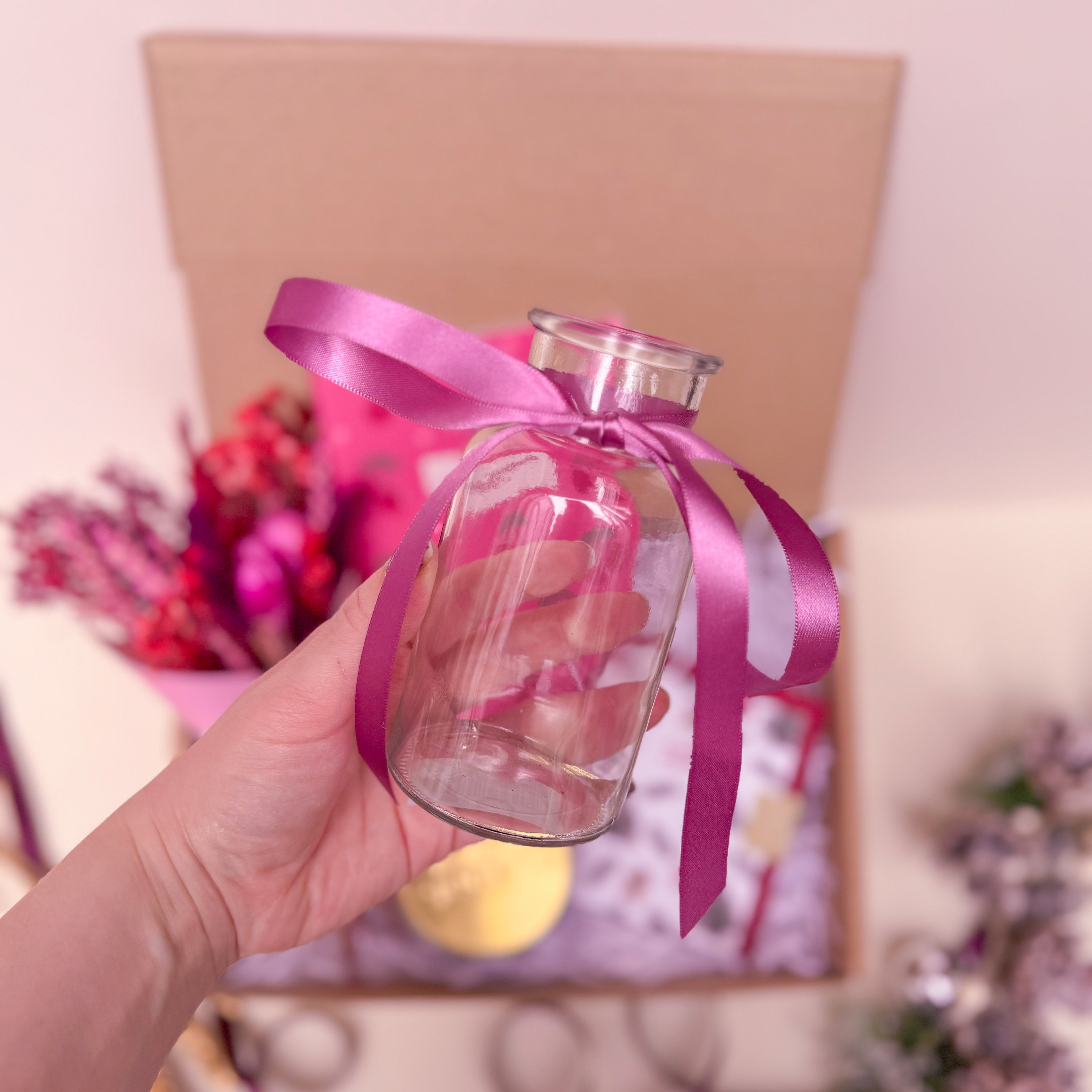 Clear glass bottle with a pink ribbon held by a hand against a blurred background