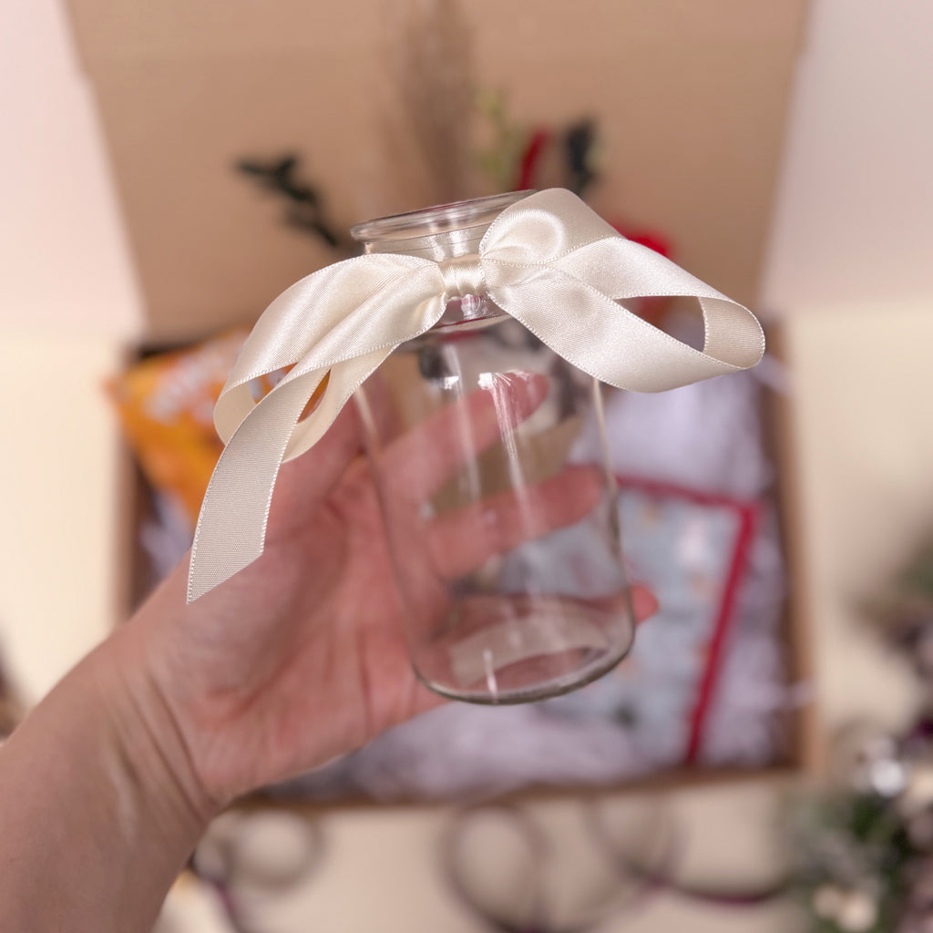 Clear glass vase with a white ribbon held by a hand against a blurred background