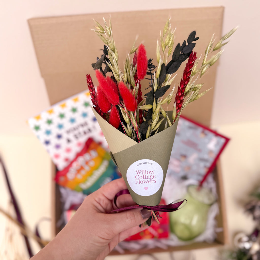 Bouquet of flowers held by a hand with 'Willow Cottage Flowers' label, blurred gift box in background