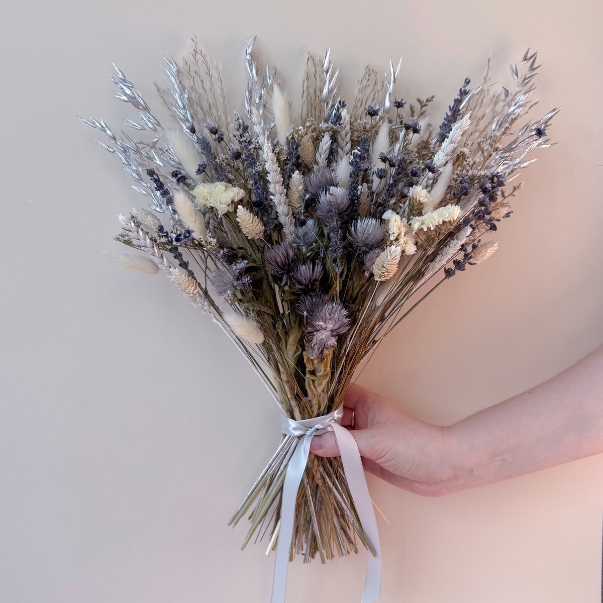 a grey and silver dried flower bouquet being held against a plain background