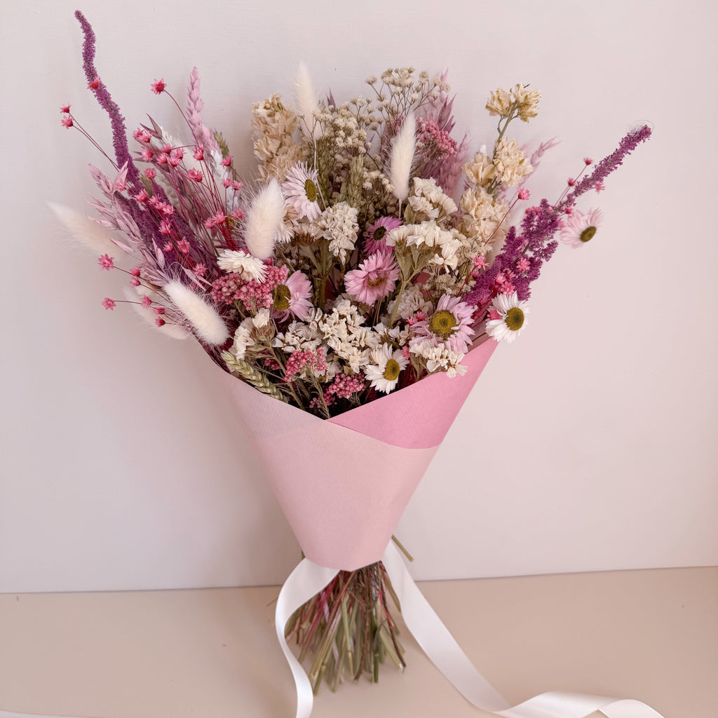 Bouquet of dried flowers wrapped in pink paper with a white ribbon on a light background