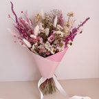 Bouquet of dried flowers wrapped in pink paper with a white ribbon on a light background