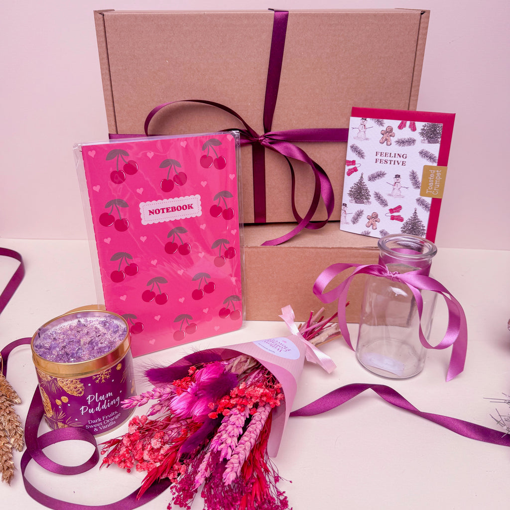 Gifting set with pink notebook, bouquet, and decorative items on a light pink background