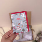 Hand holding a Christmas-themed card with festive illustrations on a neutral background