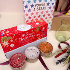 Three small tealight candles in metal tins with a decorative box labeled 'Merry Christmas'.