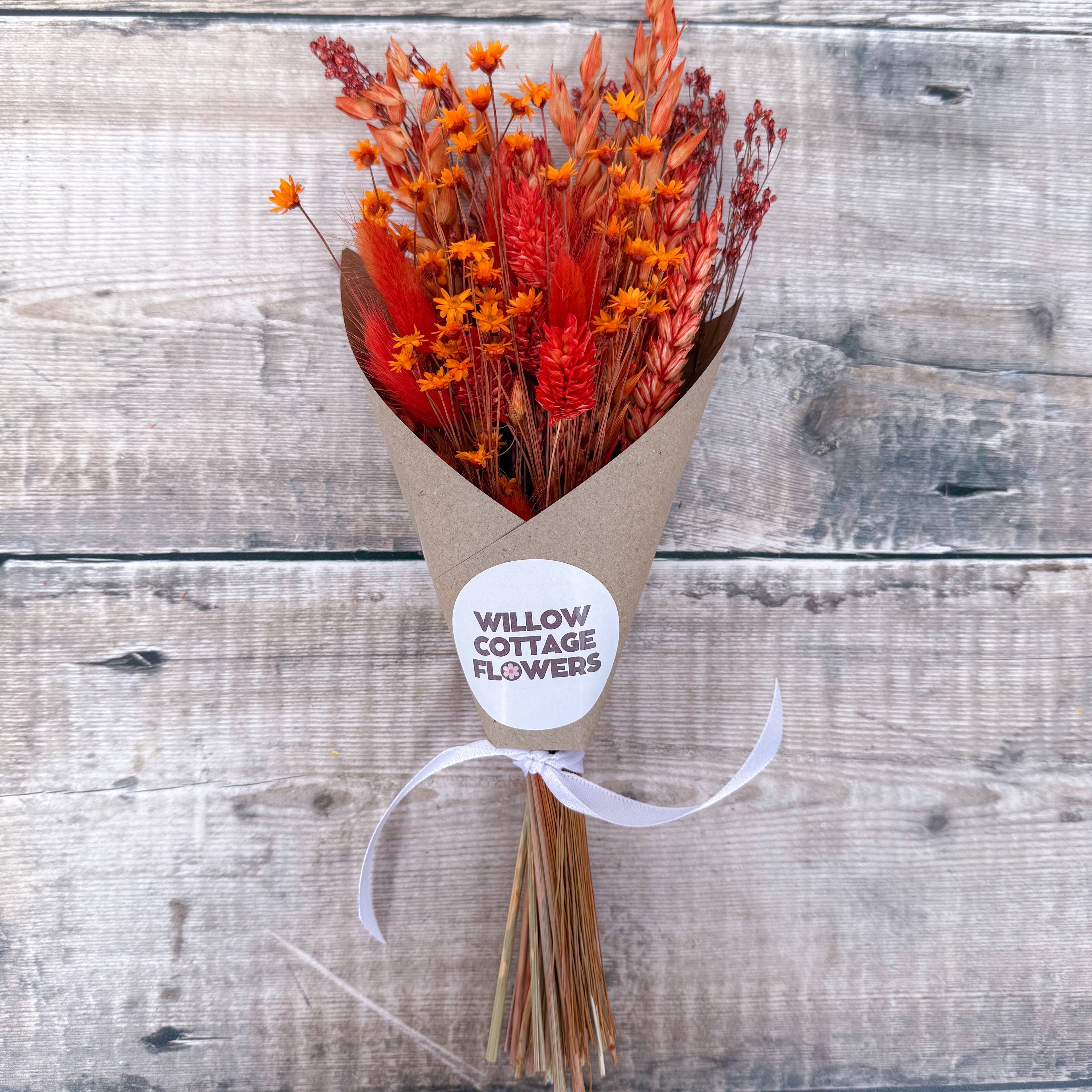 a mini burnt orange dried flower bouquet against a wooden background