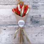 a mini burnt orange, green and white dried flower bunch against a wooden background