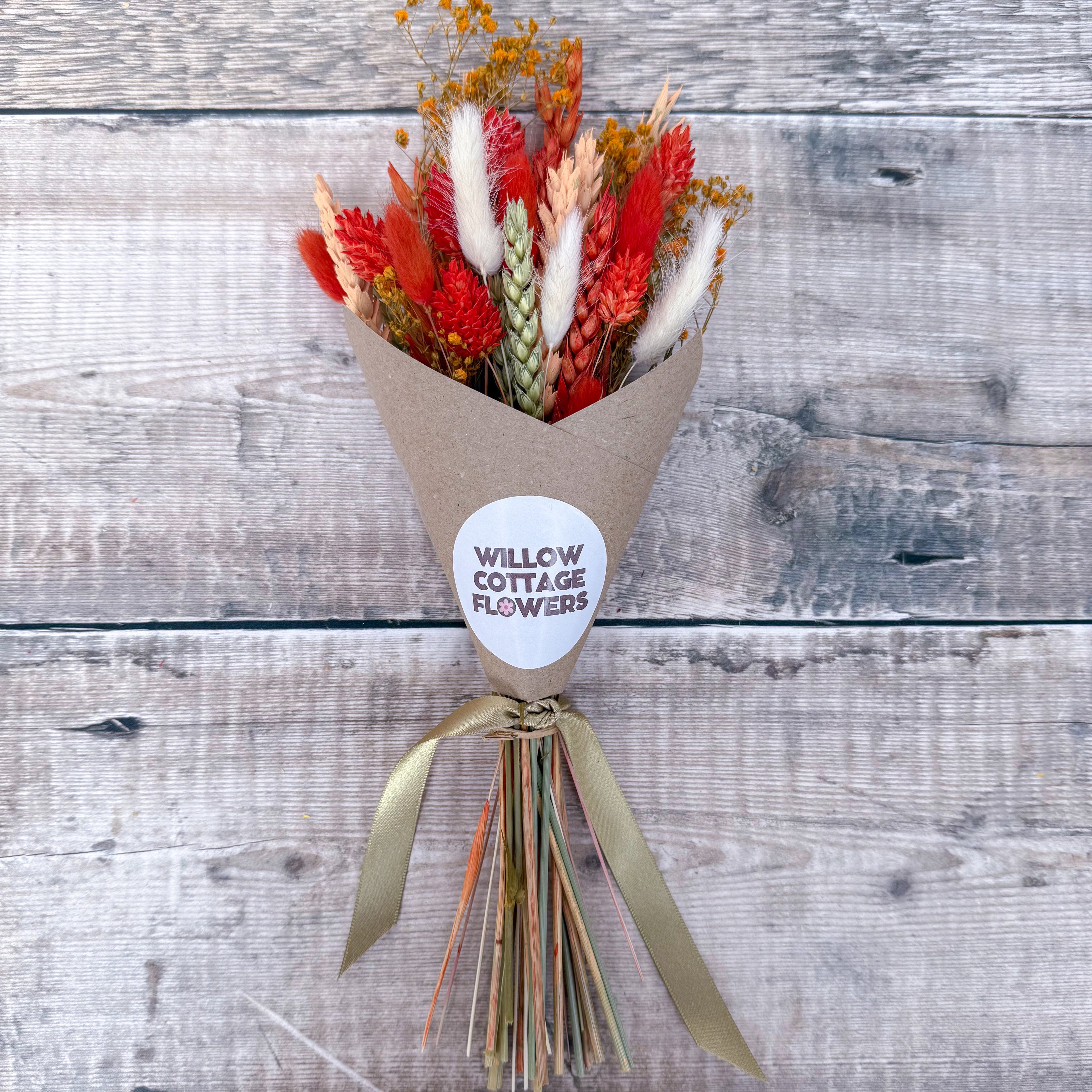 a mini burnt orange, green and white dried flower bunch against a wooden background