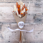 a mini white and orange dried flower bunch wrapped in brown paper against a wooden background
